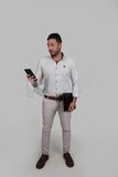 Photo Of a Handsome man standing and checking his mobile, Smiling Man, Wearing Casual Clothes Posing In a Light Room Interior, Smiling At the Camera, looking away