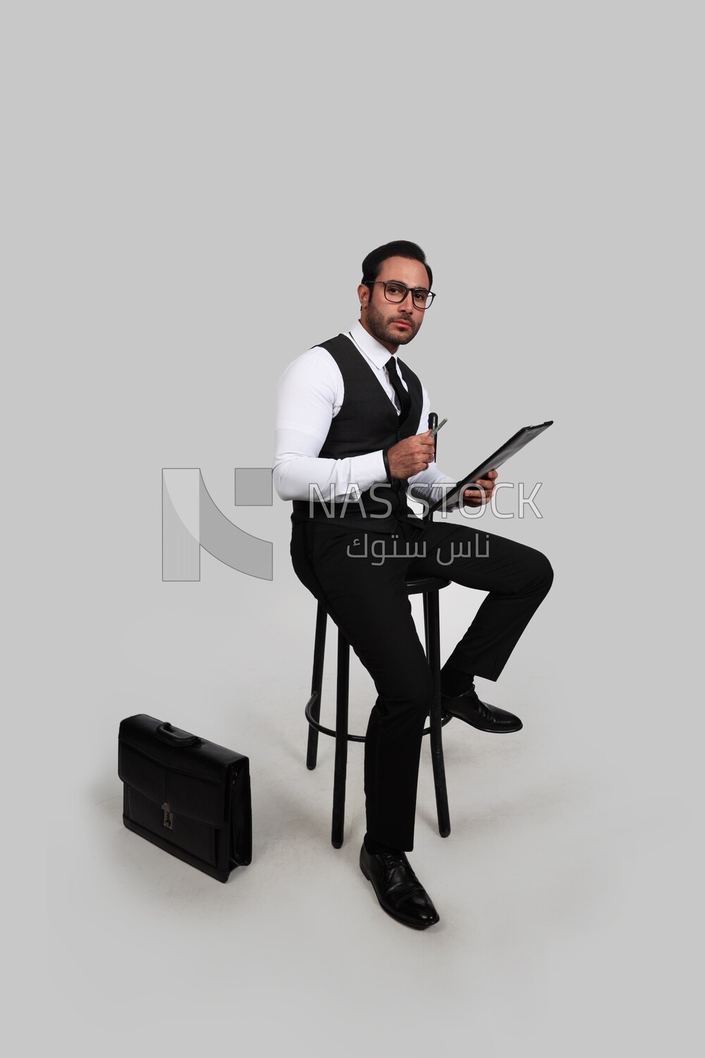 Photo of a businessman with a formal suit sitting on a chair and holding documents in one hand and a pen in the other, business development and partnerships, business meeting, Model