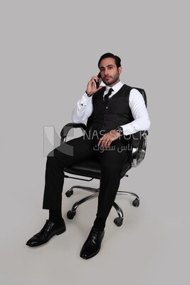 Photo of a businessman with a formal suit sitting on a chair and talking in his mobile phone, business development and partnerships, business meeting, Model