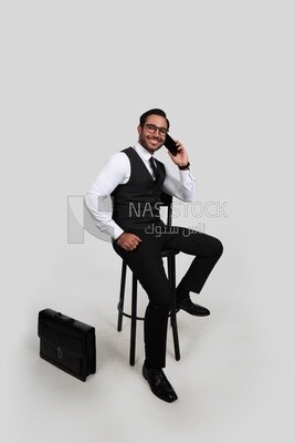 Photo of a businessman with a formal suit sitting on a chair and talking in his mobile phone, business development and partnerships, business meeting, Model