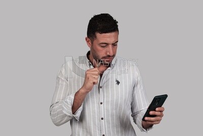 Photo Of a Handsome man standing and checking his mobile, Smiling Man, Wearing Casual Clothes Posing In a Light Room Interior, Smiling At the Camera, looking away