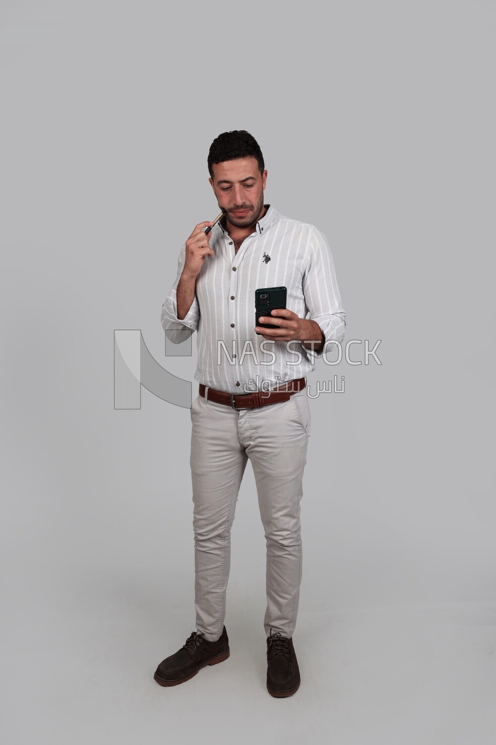 Photo Of a Handsome man standing and checking his mobile, Smiling Man, Wearing Casual Clothes Posing In a Light Room Interior, Smiling At the Camera, looking away