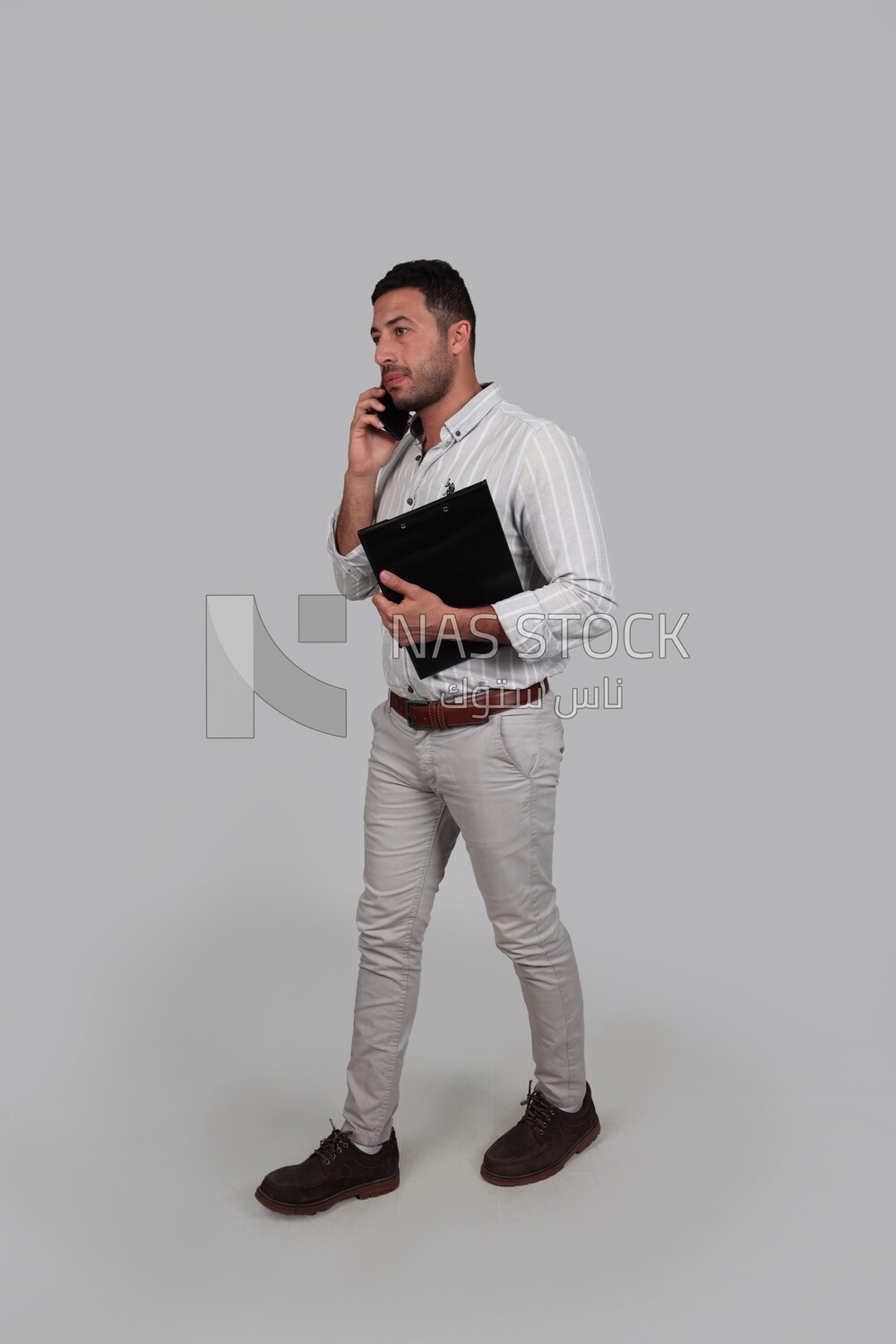 Photo Of a Handsome man standing and talking on his phone, Smiling Man, Wearing Casual Clothes Posing In a Light Room Interior, Smiling At the Camera, looking away