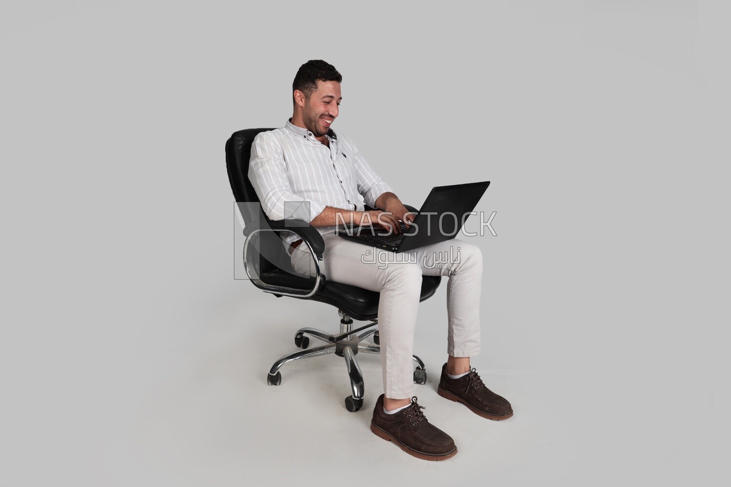 Photo Of a Handsome man sitting on a chair and working on a laptop, Smiling Man, Wearing Casual Clothes Posing In a Light Room Interior, Smiling At the Camera, looking away