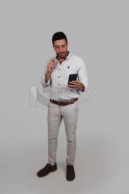 Photo Of a Handsome man standing and checking his mobile, Smiling Man, Wearing Casual Clothes Posing In a Light Room Interior, Smiling At the Camera, looking away