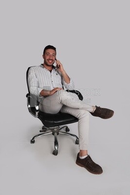 Photo Of a Handsome man sitting on a chair and talking on his phone while he puts a leg on a leg, Smiling Man, Wearing Casual Clothes Posing In a Light Room Interior, Smiling At the Camera, looking aw