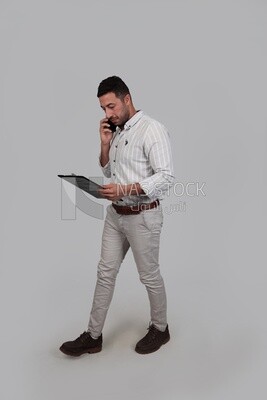 Photo Of a Handsome man talking on his mobile and holding documents, Smiling Man, Wearing Casual Clothes Posing In a Light Room Interior, Smiling At the Camera, looking away