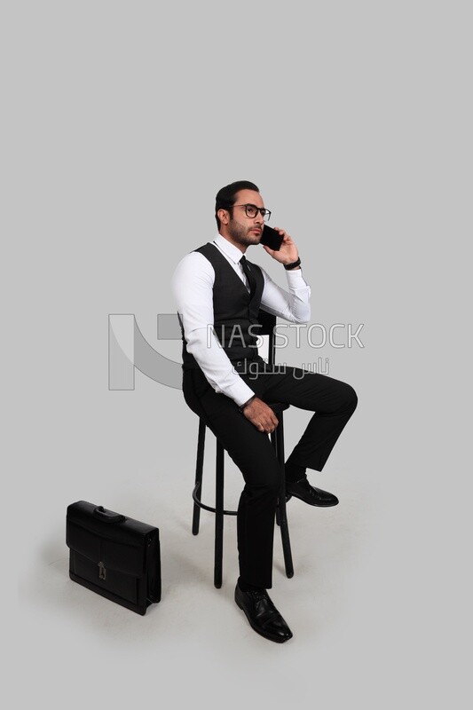 Photo of a businessman with a formal suit sitting on a chair and talking in his mobile phone, business development and partnerships, business meeting, Model