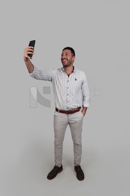 Photo Of a Handsome man standing and taking a selfie, Smiling Man, Wearing Casual Clothes Posing In a Light Room Interior, Smiling At the Camera, looking away