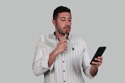 Photo Of a Handsome man standing and checking his mobile, Smiling Man, Wearing Casual Clothes Posing In a Light Room Interior, Smiling At the Camera, looking away