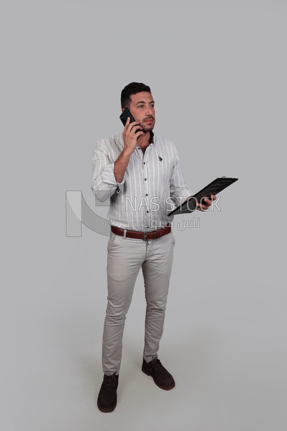 Photo Of a Handsome man talking on his mobile and holding documents, Smiling Man, Wearing Casual Clothes Posing In a Light Room Interior, Smiling At the Camera, looking away