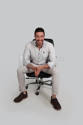 Photo Of a Handsome man sitting on a chair, Smiling Man, Wearing Casual Clothes Posing In a Light Room Interior, Smiling At the Camera, looking away