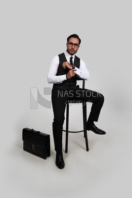 Photo of a businessman with a formal suit sitting on a chair and looking at the camera, business development and partnerships, business meeting, Model