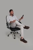 Photo Of a Handsome man sitting on a chair checking his mobile, Smiling Man, Wearing Casual Clothes Posing In a Light Room Interior, Smiling At the Camera, looking away