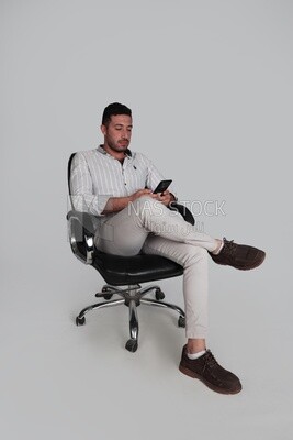 Photo Of a Handsome man sitting on a chair checking his mobile, Smiling Man, Wearing Casual Clothes Posing In a Light Room Interior, Smiling At the Camera, looking away