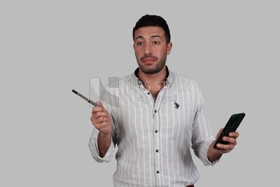 Photo Of a Handsome man standing and checking his mobile, Smiling Man, Wearing Casual Clothes Posing In a Light Room Interior, Smiling At the Camera, looking away