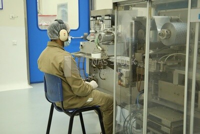 Worker at a machine in a factory wears a mask and a head cover