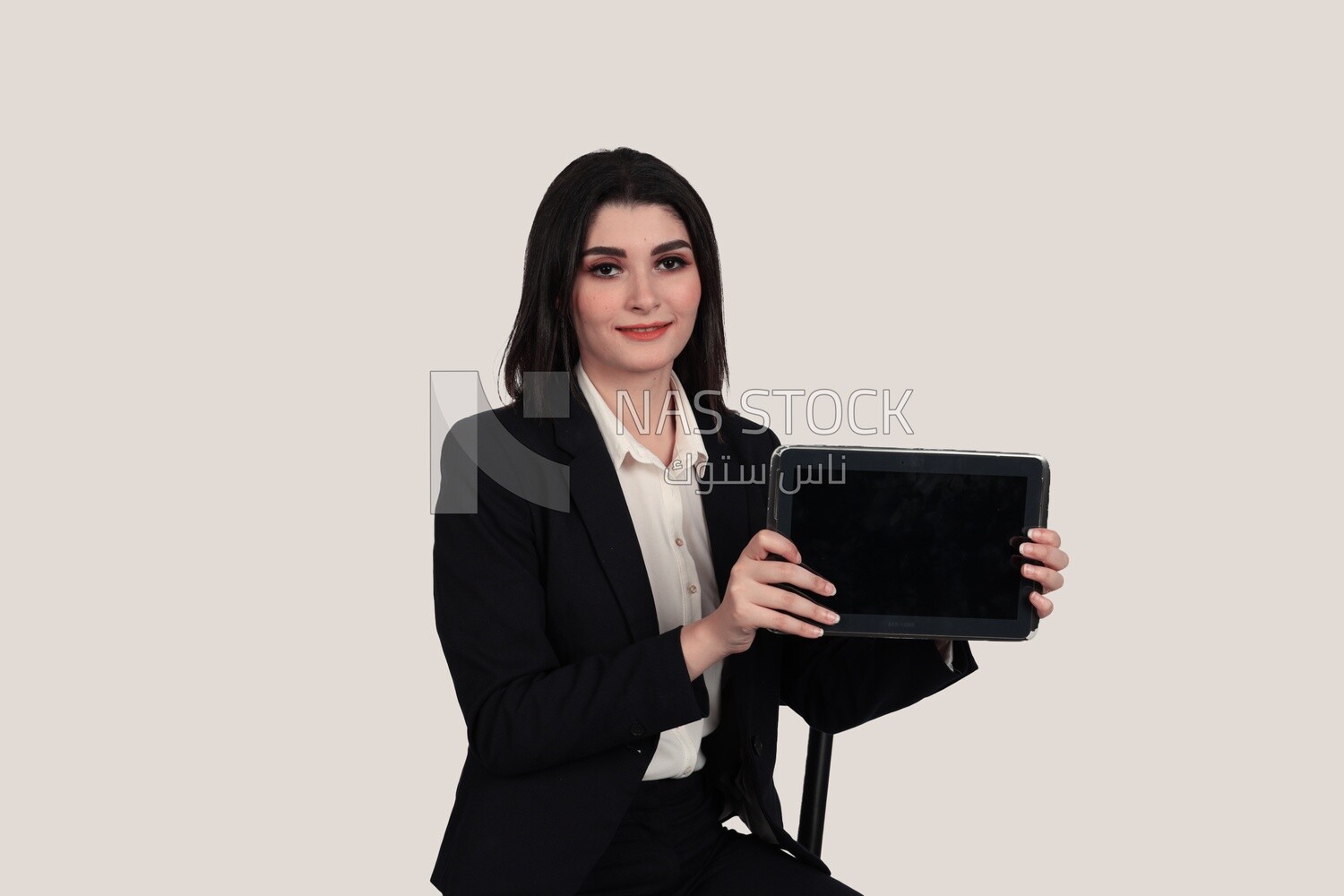 Photo of a businesswoman with a formal suit sitting on a chair and holding a tablet, business development and partnerships, business meeting, Model