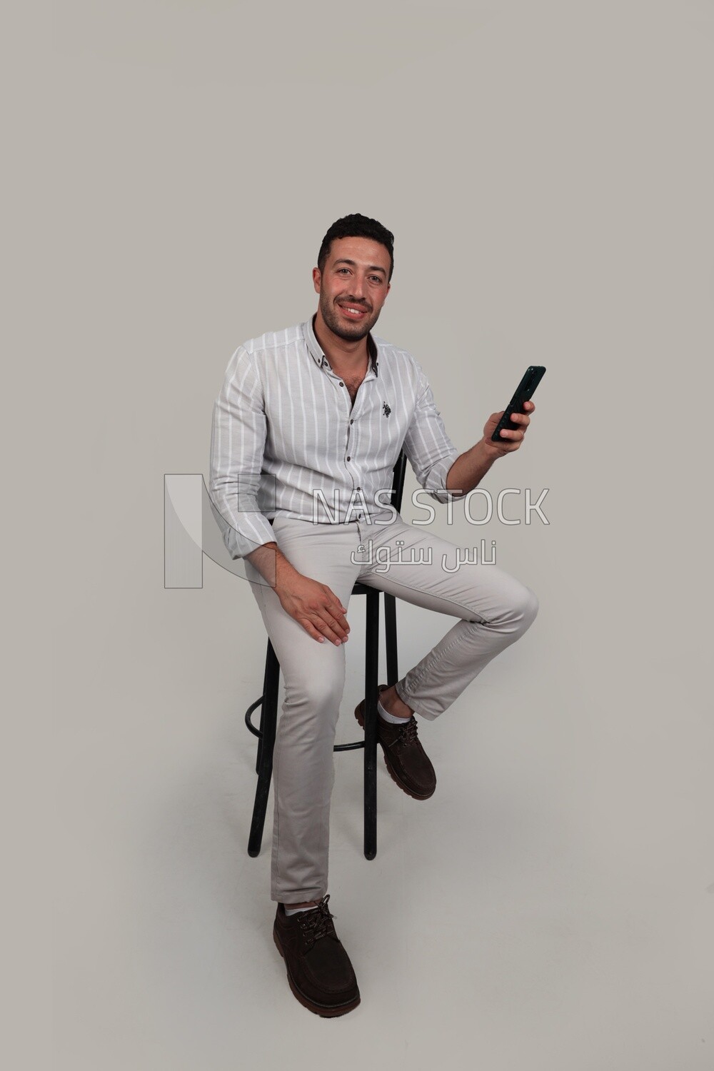 Photo Of a Handsome man sitting and checking his mobile, Smiling Man, Wearing Casual Clothes Posing In a Light Room Interior, Smiling At the Camera, looking away