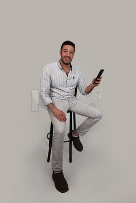 Photo Of a Handsome man sitting and checking his mobile, Smiling Man, Wearing Casual Clothes Posing In a Light Room Interior, Smiling At the Camera, looking away