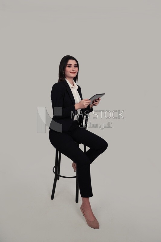 Photo of a businesswoman with a formal suit sitting on a chair and holding a tablet, business development and partnerships, business meeting, Model