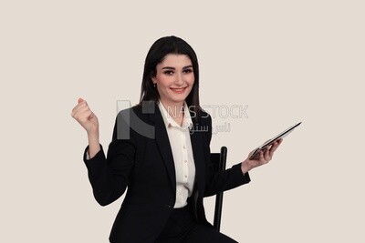 Photo of a businesswoman with a formal suit sitting on a chair and holding a tablet looks like she is happy, business development and partnerships, business meeting, Model