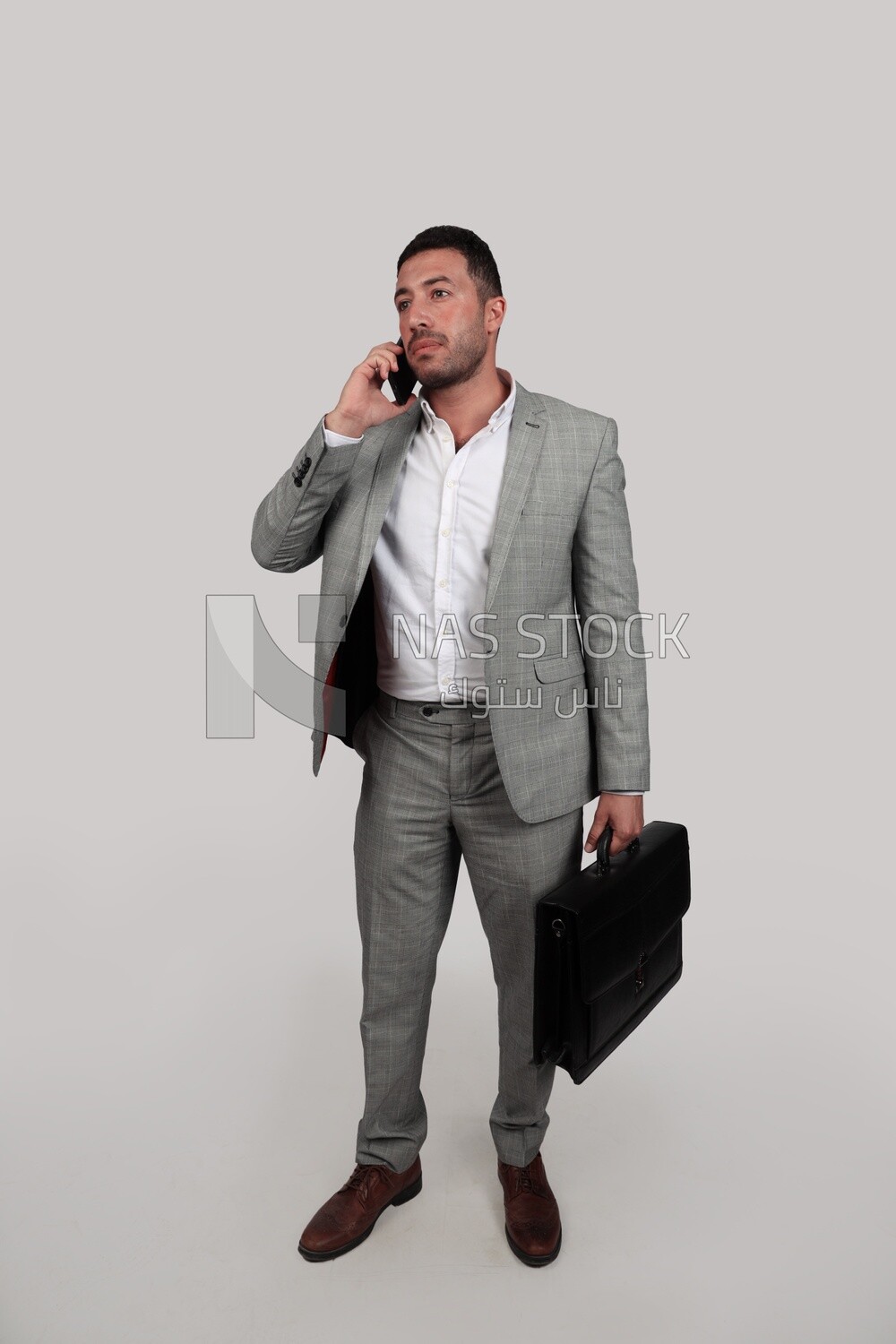 Photo of a businessman with formal wear holding a leather bag while talking on the phone, business development and partnerships, business meeting, Model