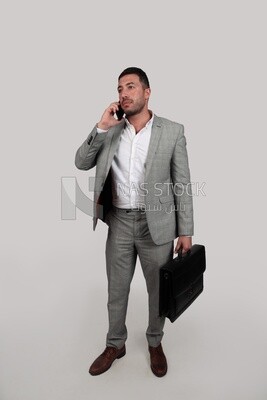 Photo of a businessman with formal wear holding a leather bag while talking on the phone, business development and partnerships, business meeting, Model