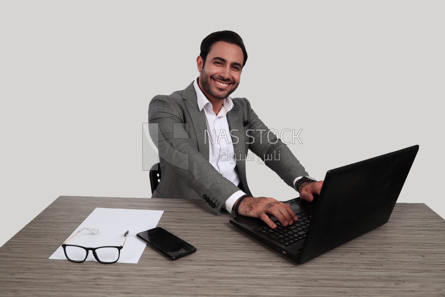 Photo of a businessman with a formal suit sitting at a desk working on a laptop looking happy, business development and partnerships, business meeting, Model