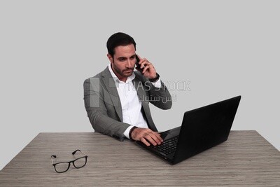 Photo of a businessman with a formal suit sitting at a desk working on a laptop while talking on the phone, business development and partnerships, business meeting, Model