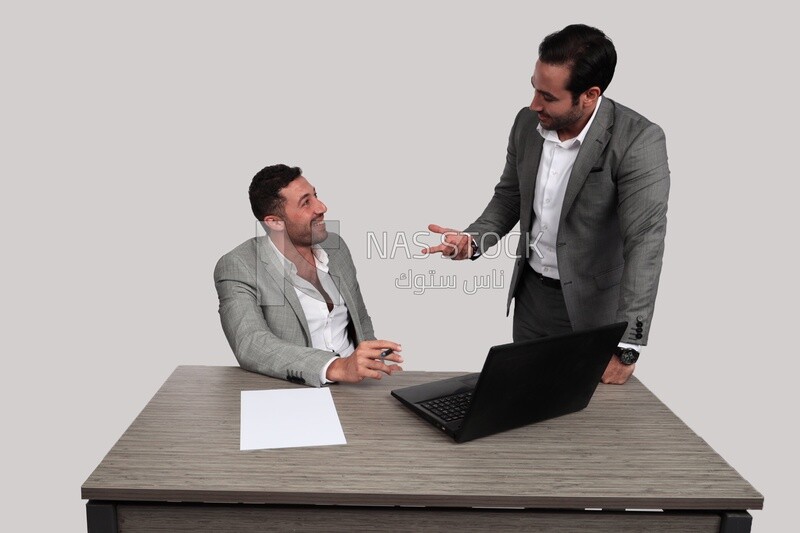 Photo of two men one sitting in the office and the other standing, discussing the work, business development and partnerships, business meeting, Model