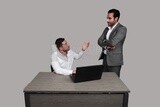 Photo of two men one sitting in the office and the other standing, discussing the work, business development and partnerships, business meeting, Model