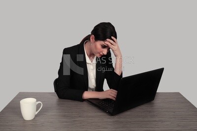 Photo of a businesswoman with a formal suit sitting at a desk working on a laptop looking tired, business development and partnerships, business meeting, Model