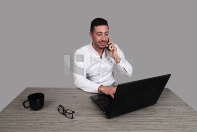 Photo of a businessman with a formal suit sitting at a desk working on a laptop while talking on his mobile, business development and partnerships, business meeting, Model