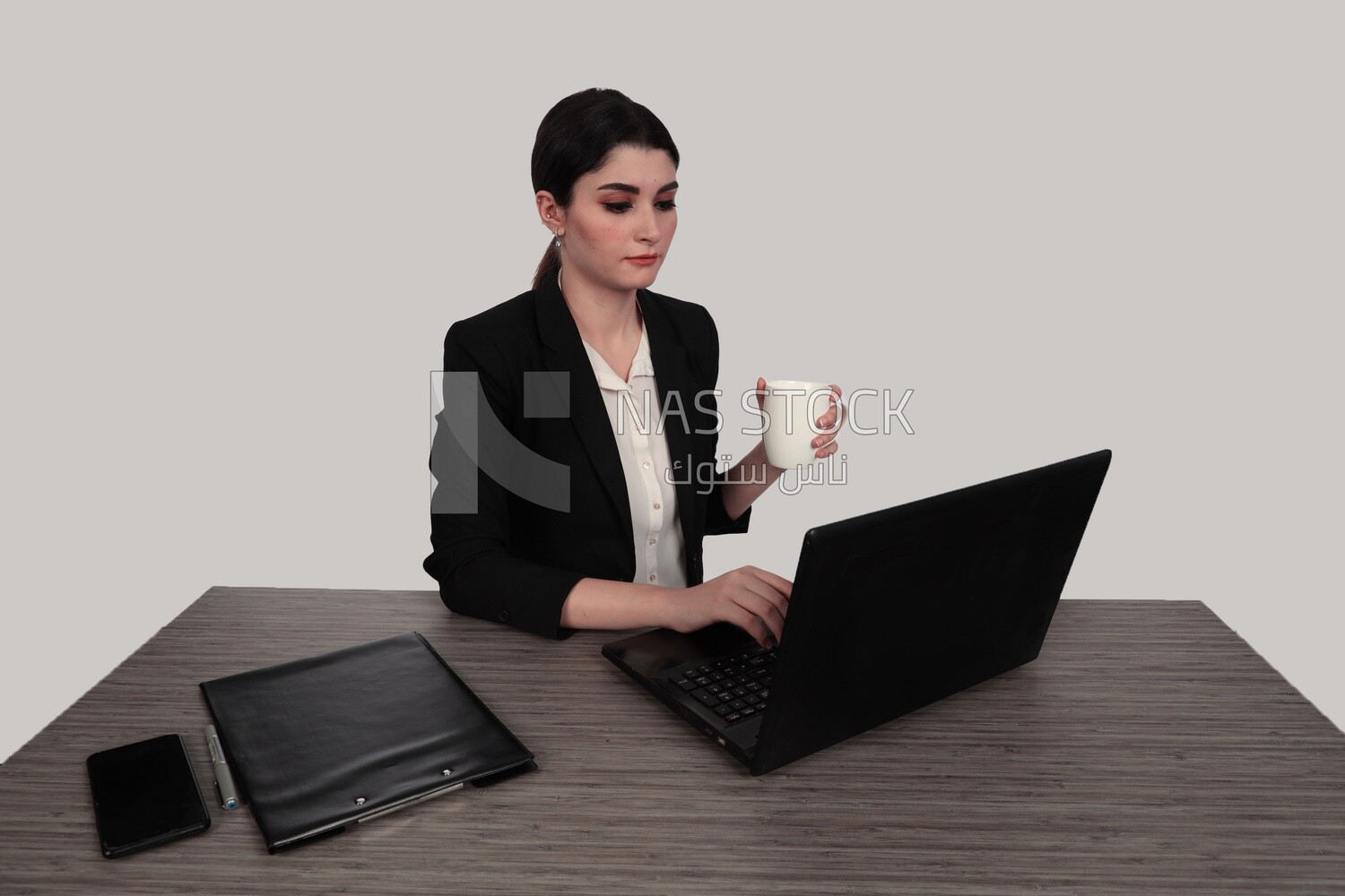 Photo of a businesswoman with a formal suit sitting at a desk drinking coffee while she works on a laptop, business development and partnerships, business meeting, Model