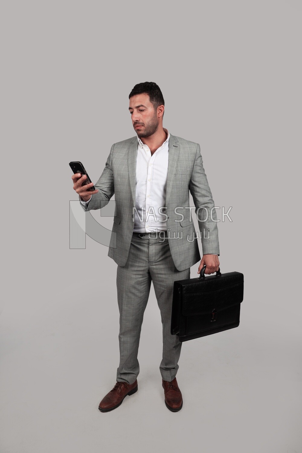 Photo of a businessman with a formal suit holding a leather bag and checking his mobile, business development and partnerships, business meeting, Model
