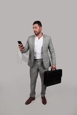 Photo of a businessman with a formal suit holding a leather bag and checking his mobile, business development and partnerships, business meeting, Model