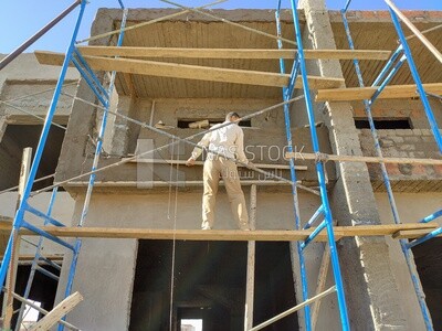 عامل يقف على سقالة , في موقع البناء