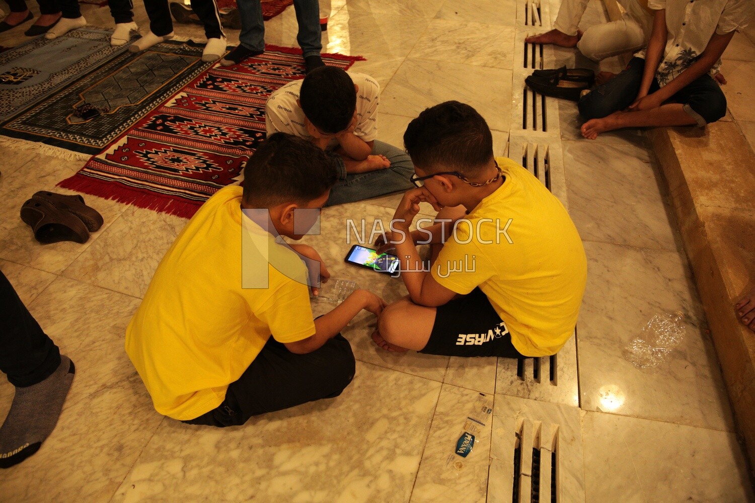 Boys in the mosque, watching the mobile, praying on the prayer rug, performing the obligatory prayer in the mosque, worship and draw close to God