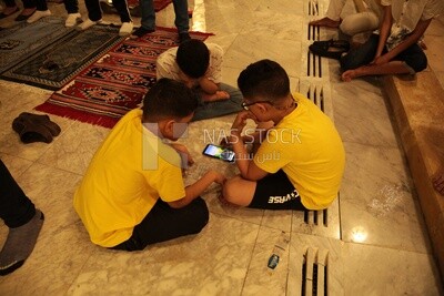 Boys in the mosque, watching the mobile, praying on the prayer rug, performing the obligatory prayer in the mosque, worship and draw close to God