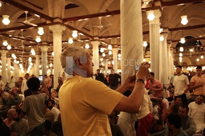 Man in the mosque, holding his mobile, praying on the prayer rug, performing the obligatory prayer in the mosque, worship and draw close to God