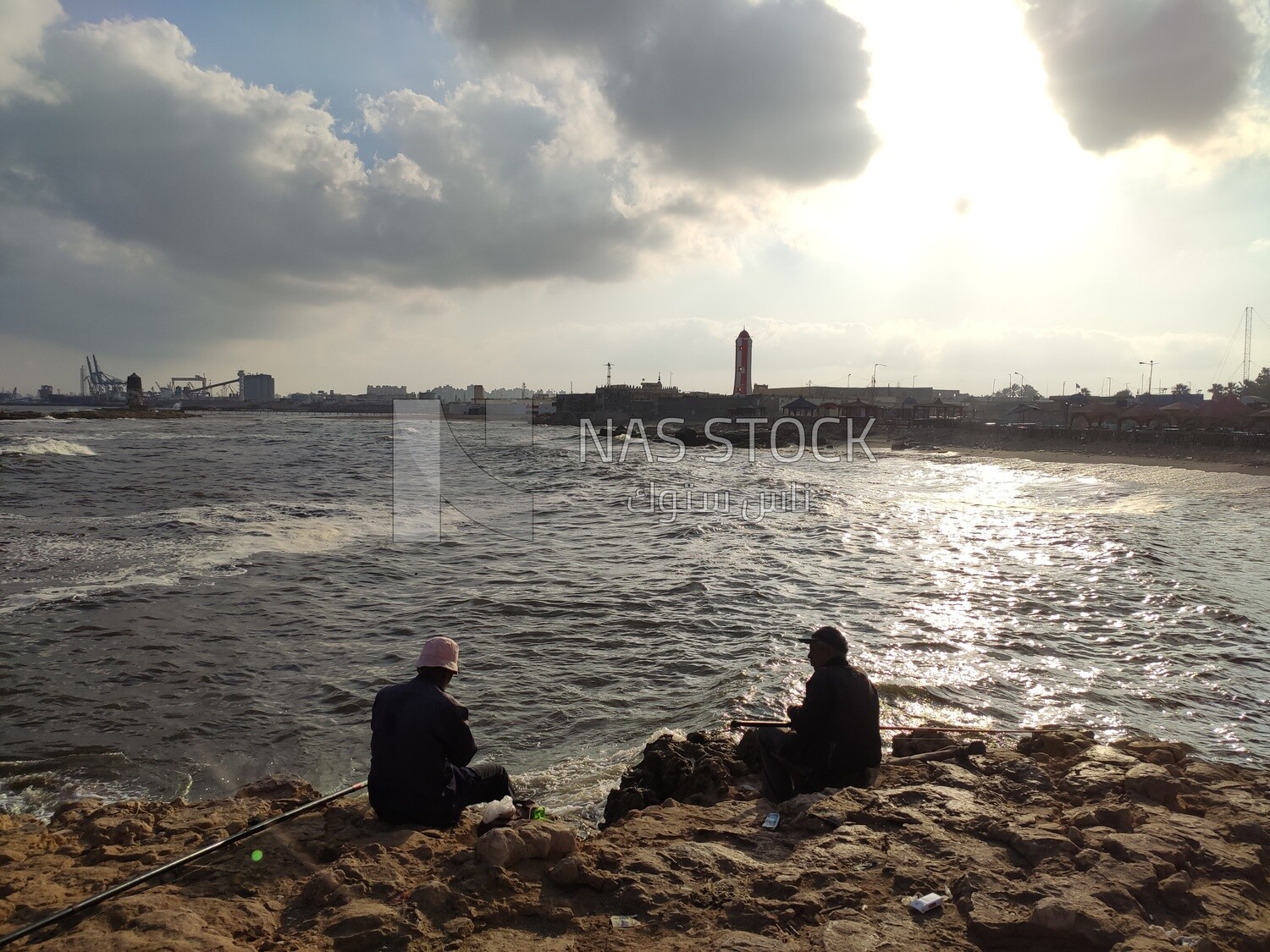 Two men sitting on the seashore enjoying fishing