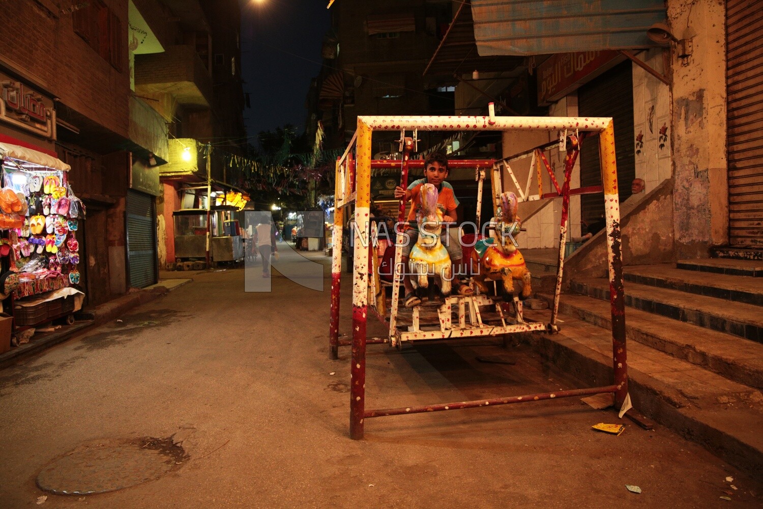 Boy sitting on the swing in the street, Ramadan nights