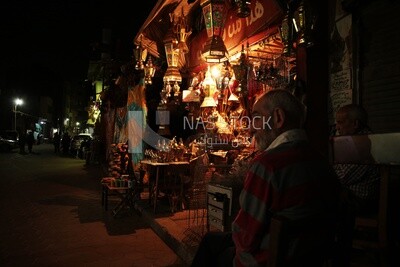 Two men sitting in front of a street shop drinking hookah, street, decoration lights