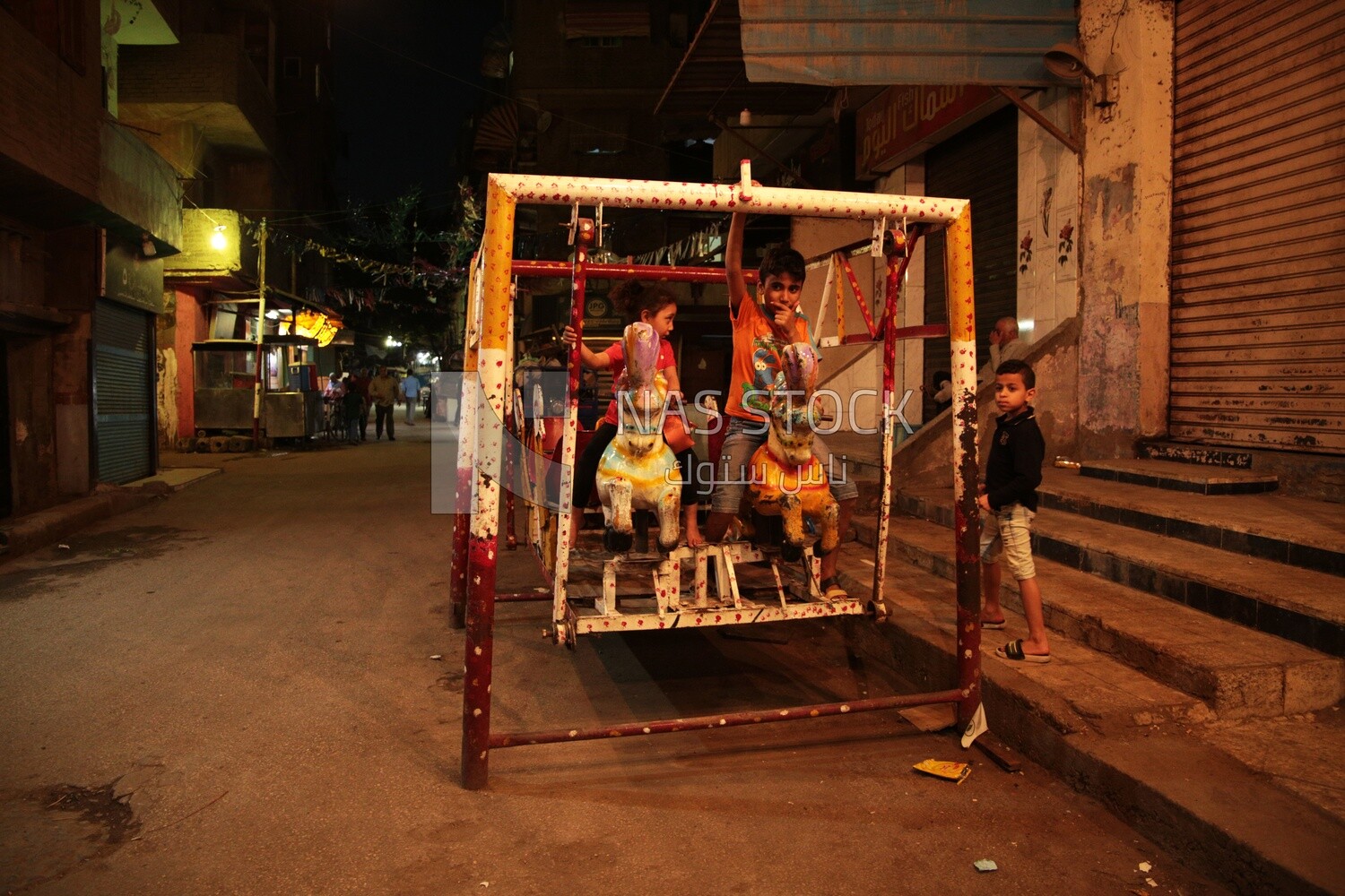Boy sitting on the swing in the street, Ramadan nights
