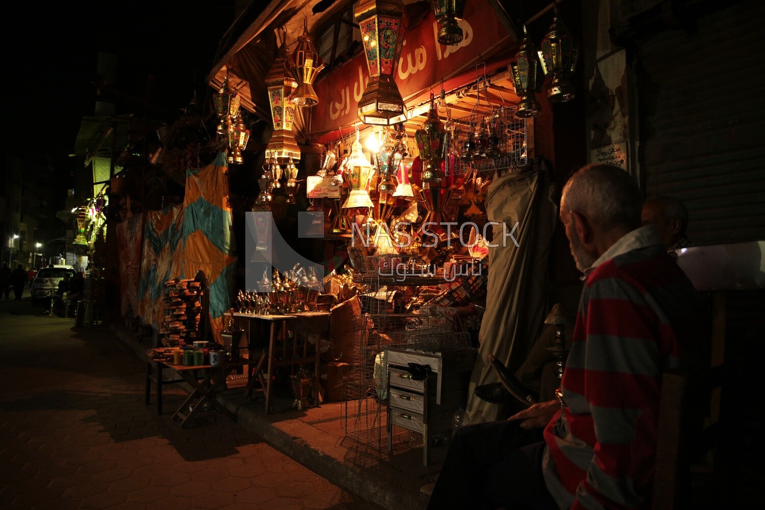 Two men sitting in front of a street shop drinking hookah, street, decoration lights