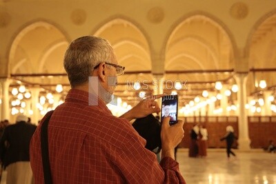 Man in the mosque, holding his mobile, praying on the prayer rug, performing the obligatory prayer in the mosque, worship and draw close to God