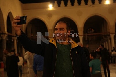 Man in the mosque, holding his mobile, praying on the prayer rug, performing the obligatory prayer in the mosque, worship and draw close to God