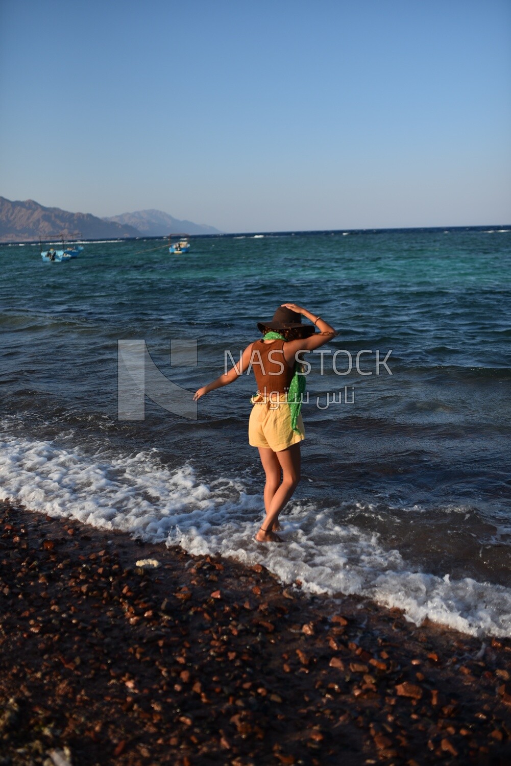Woman wearing summer clothes and a straw hat stands in front of the sea