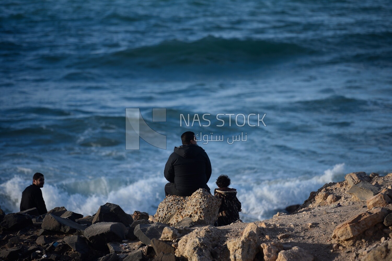 Man sits with his child on a rock on the beach